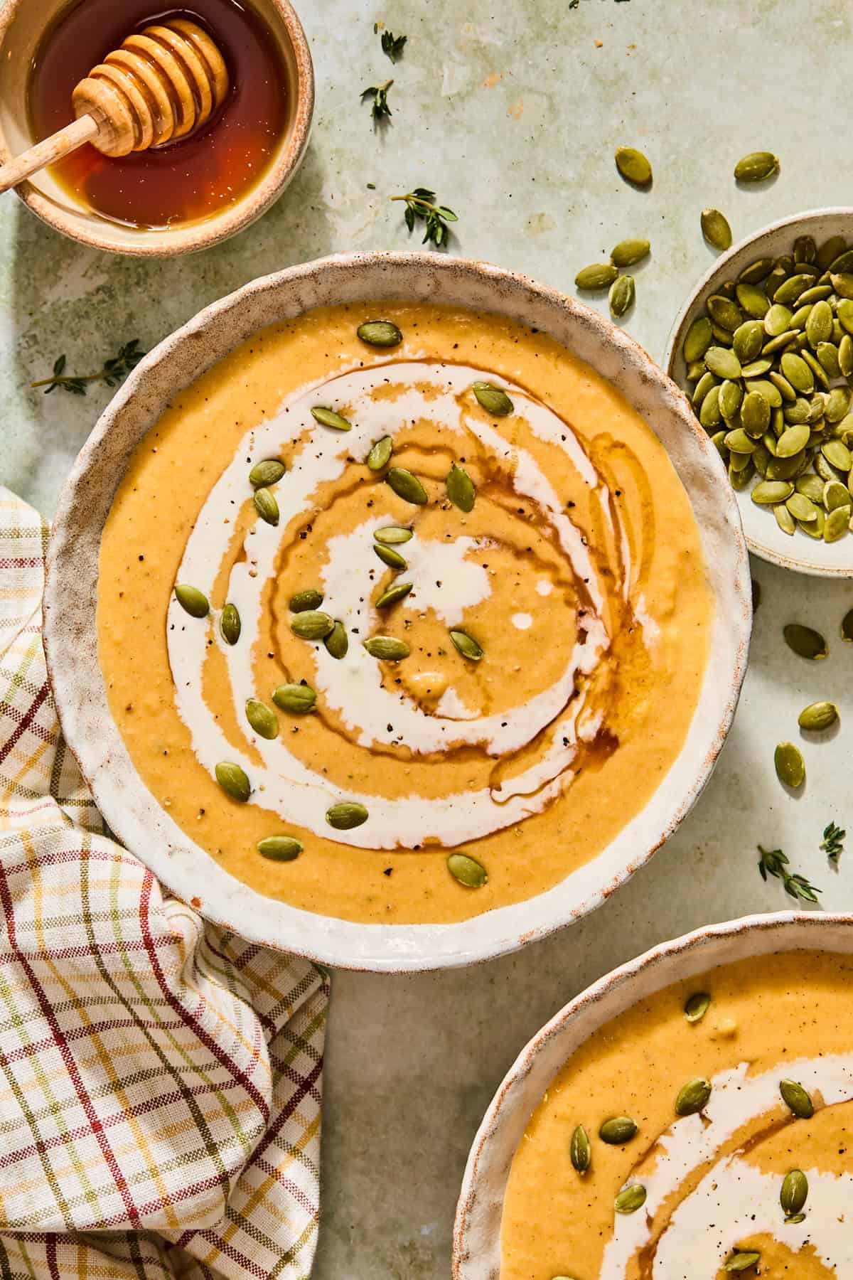 Roasted butternut squash soup in a bowl topped with pumpkin seeds and a drizzle of cream next to a bowl of honey and pumpkin seeds.