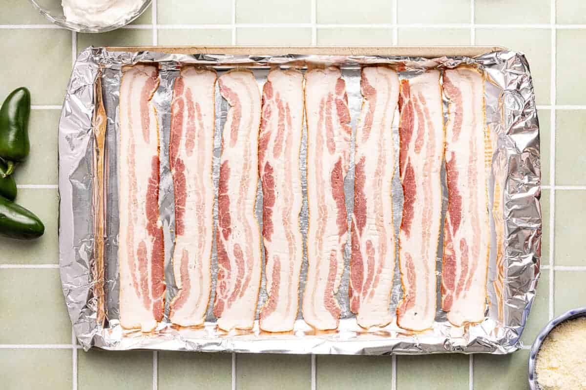 Slices of raw bacon on a foiled baking sheet.