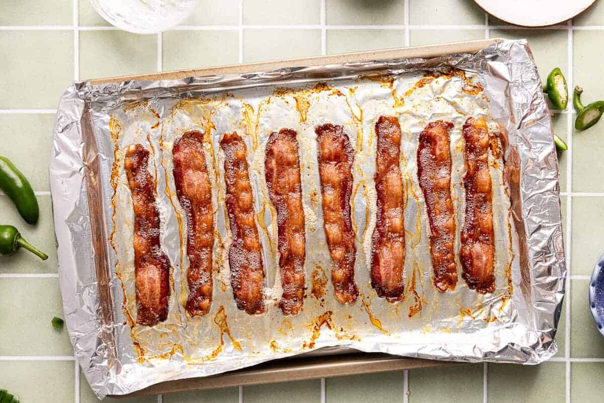 Slices of cooked bacon on a foil lined baking sheet.