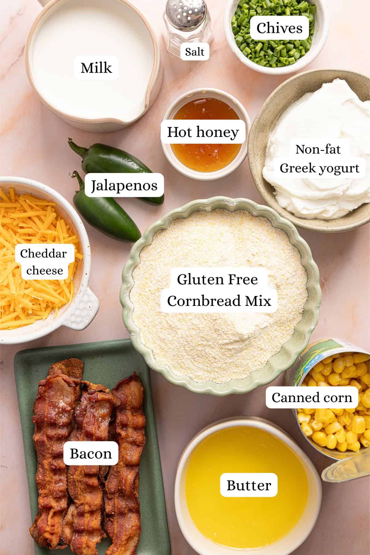 Ingredients for cornbread casserole in bowls: gluten free cornbread mix, Greek yogurt, milk, butter, canned corn, bacon, cheddar, jalapenos, hot honey, and chives