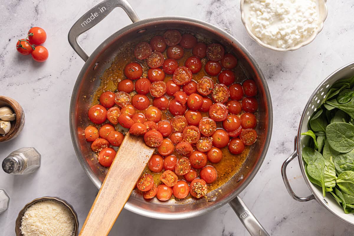 Cooking whole cherry tomatoes in a pot with spices.