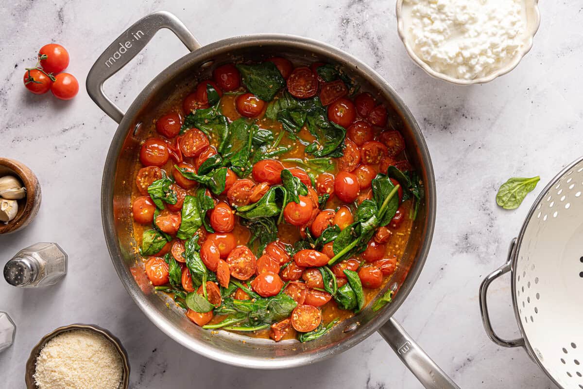 Spinach cooking in a pot of cherry tomatoes and seasonings.
