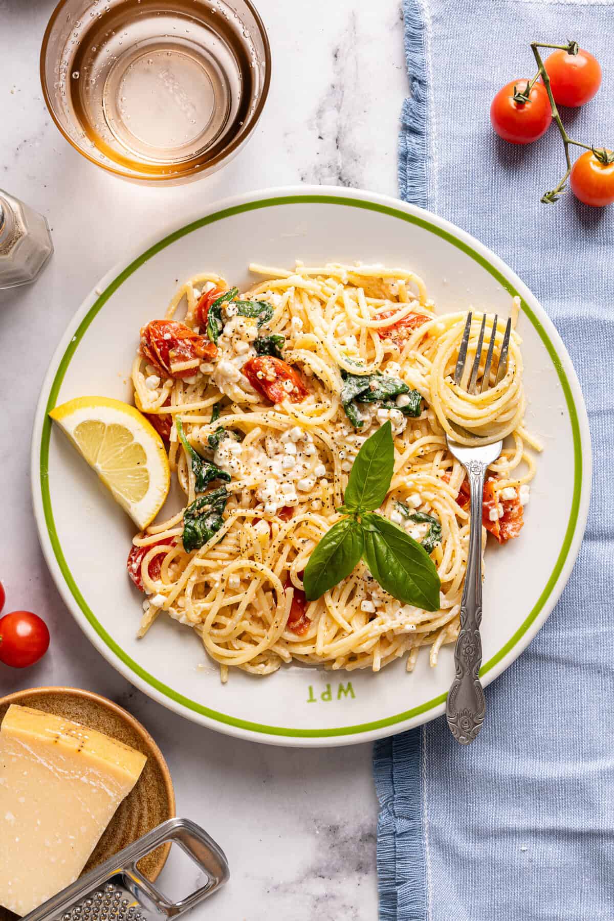 An overhead shot of a serving of cottage cheese pasta with spinach and tomatoes on a plate topped with fresh basil and a lemon wheel.