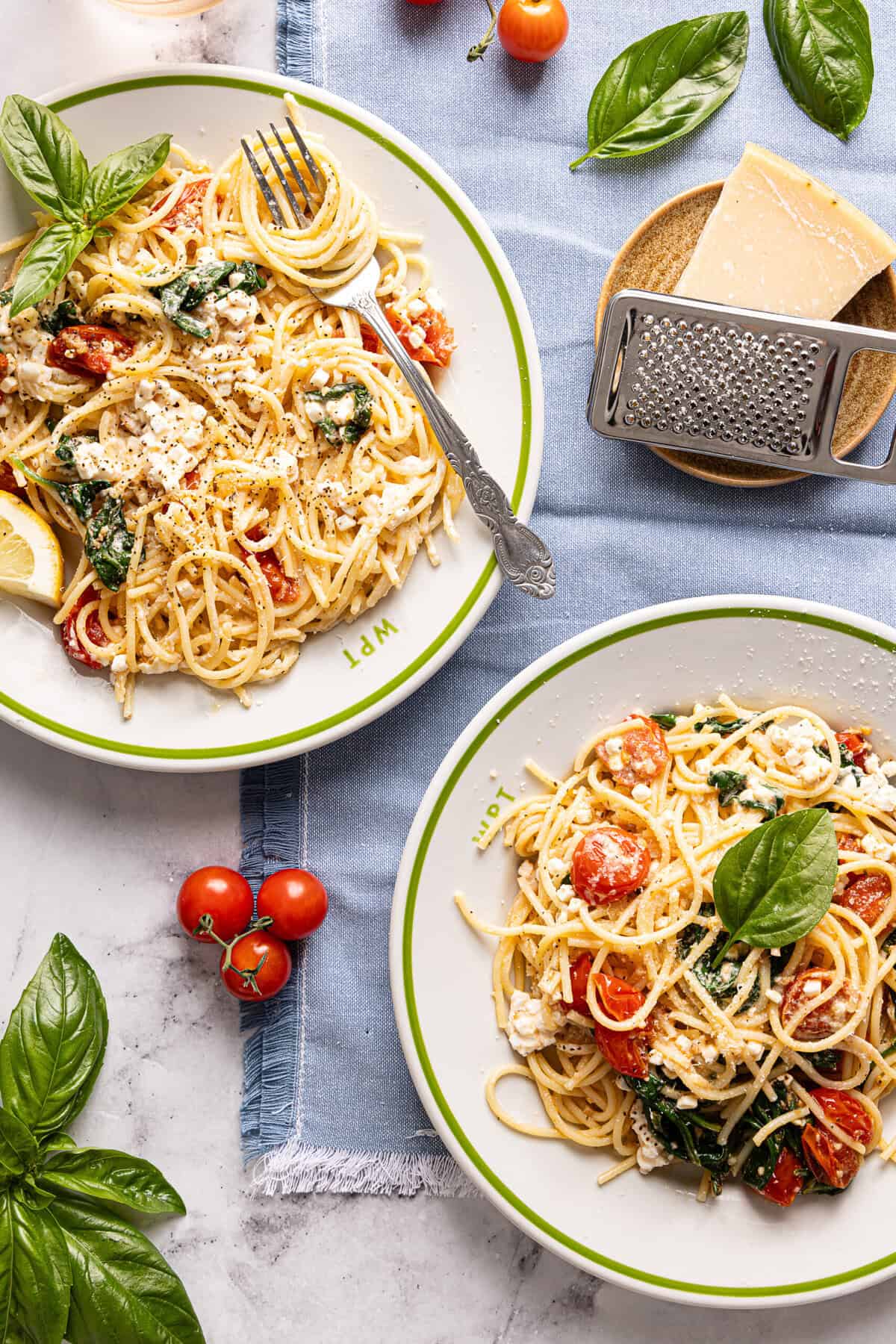 Two plates topped with cottage cheese pasta: spaghetti noodles, tomatoes, spinach, and cottage cheese.