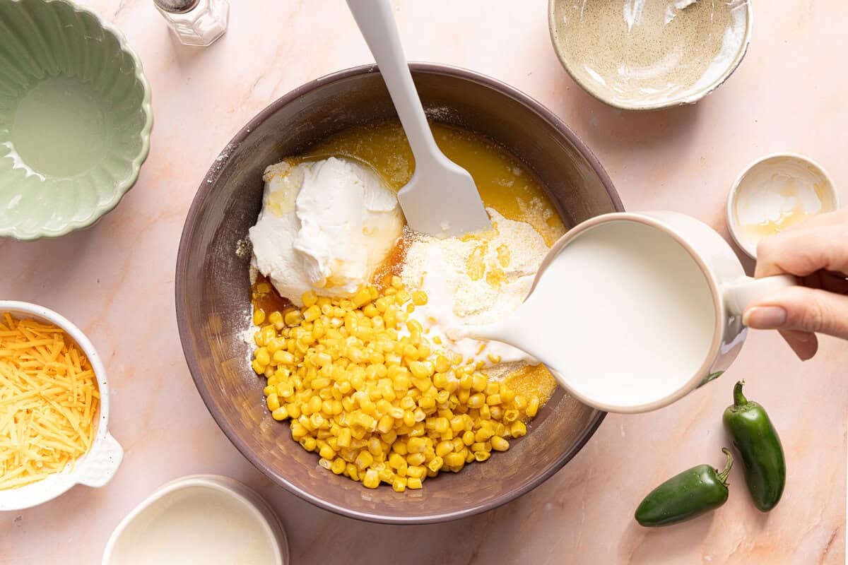 Adding the cornbread casserole ingredients to a mixing bowl before combining.
