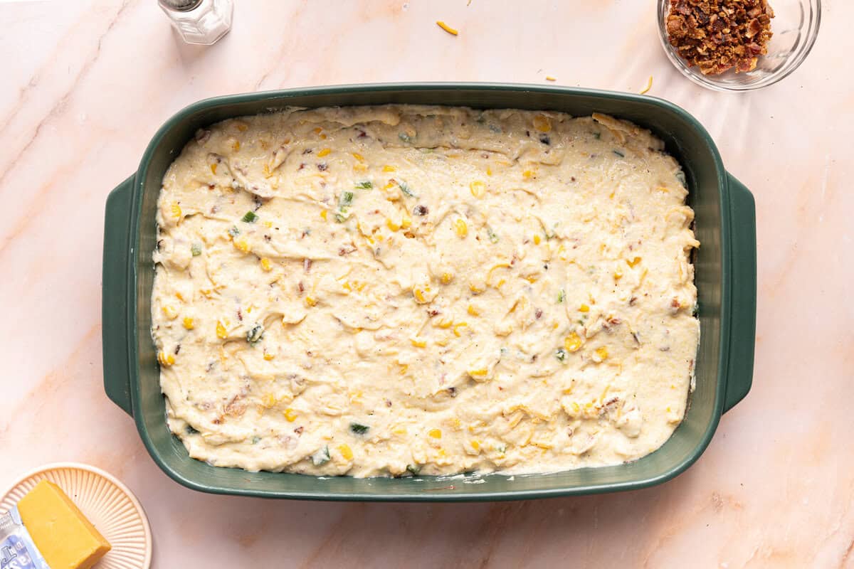 The cornbread casserole batter spread across a 9x13 inch green pan