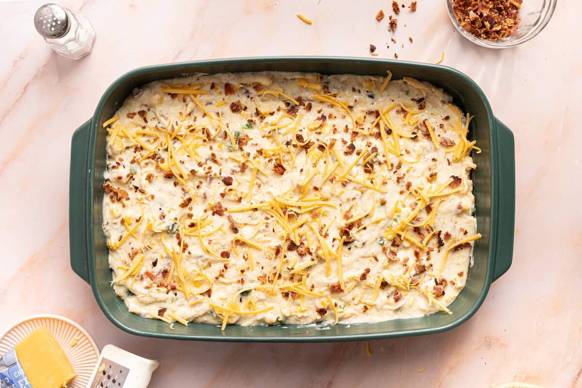 Topping the cornbread casserole batter with chopped bacon and shredded cheese.