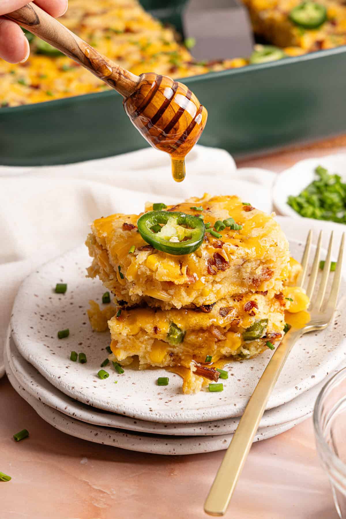 Two squares of cornbread casserole stacked on a plate with hot honey drizzled over the top