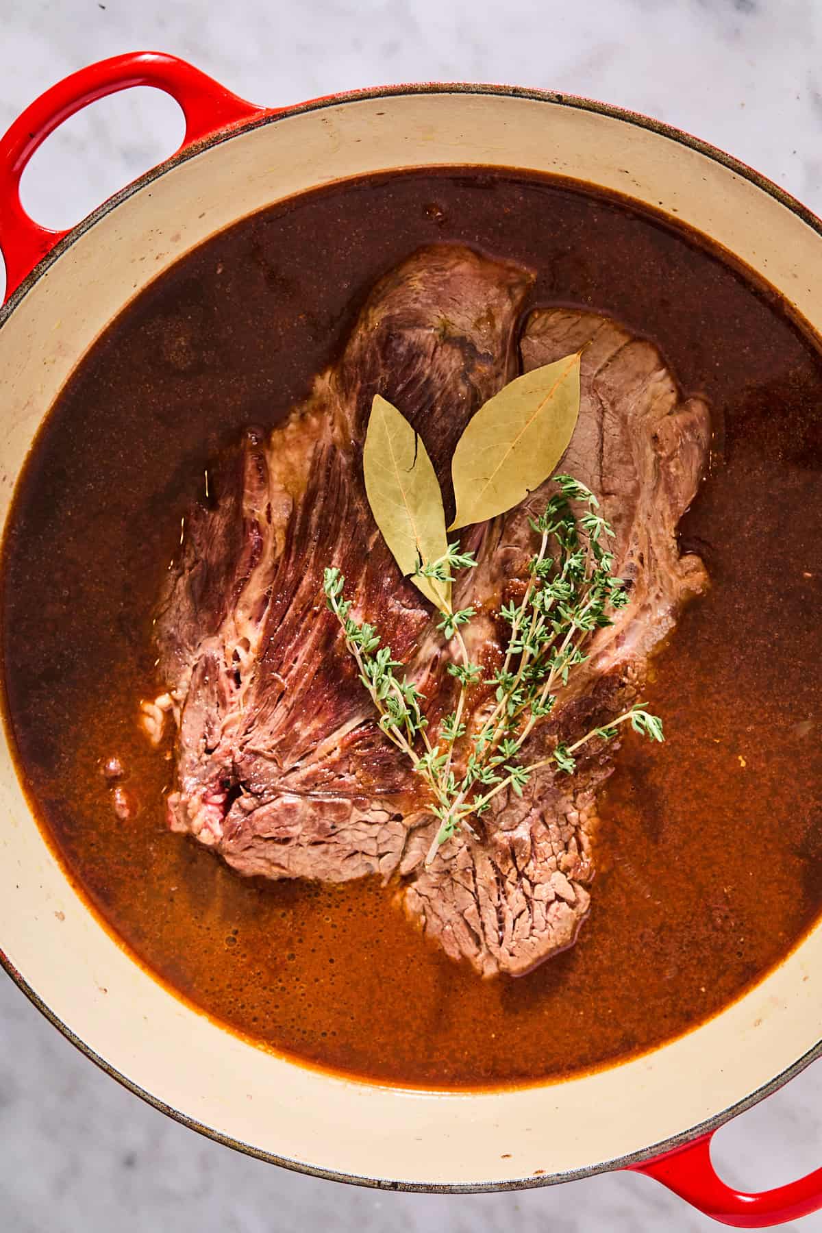 Broth, red wine, and fresh herbs in a Dutch oven along with the seared chuck roast to make a pot roast.