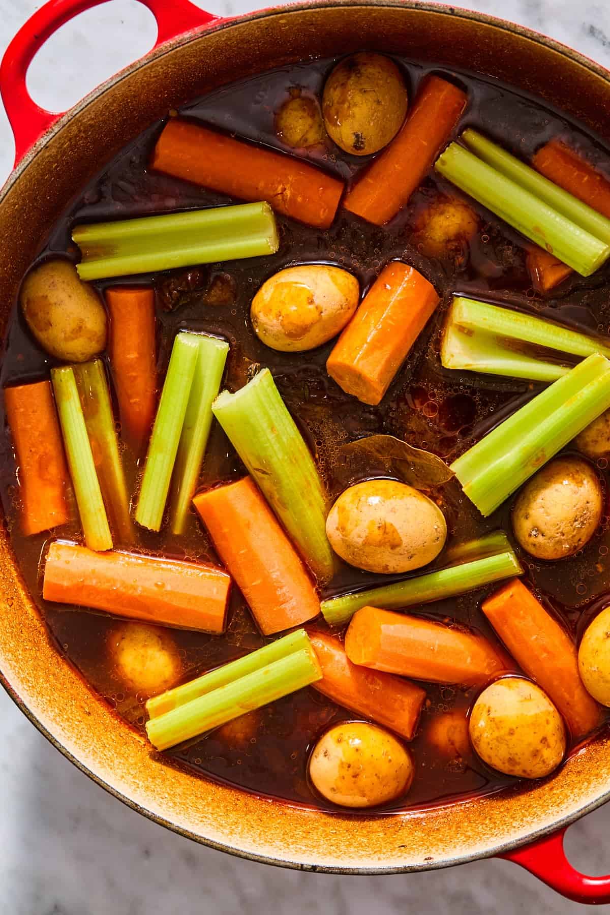 Raw celery, carrots, and potatoes added to the Dutch oven pot roast.
