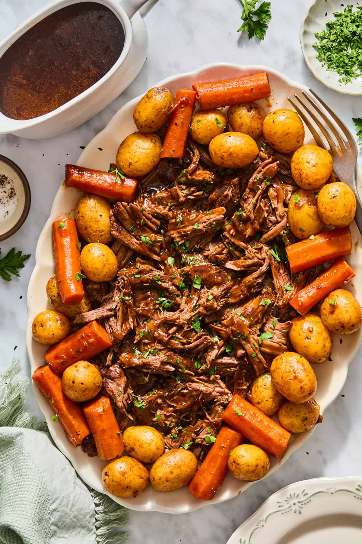Dutch oven pot roast shredded on a platter with potatoes and carrots