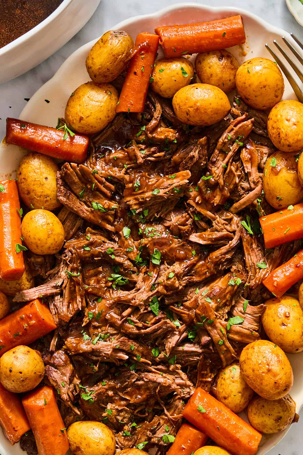 A close up photo of shredded beef, cooked potatoes, and cooked carrots on a plate topped with gravy made from a Dutch oven pot roast recipe.