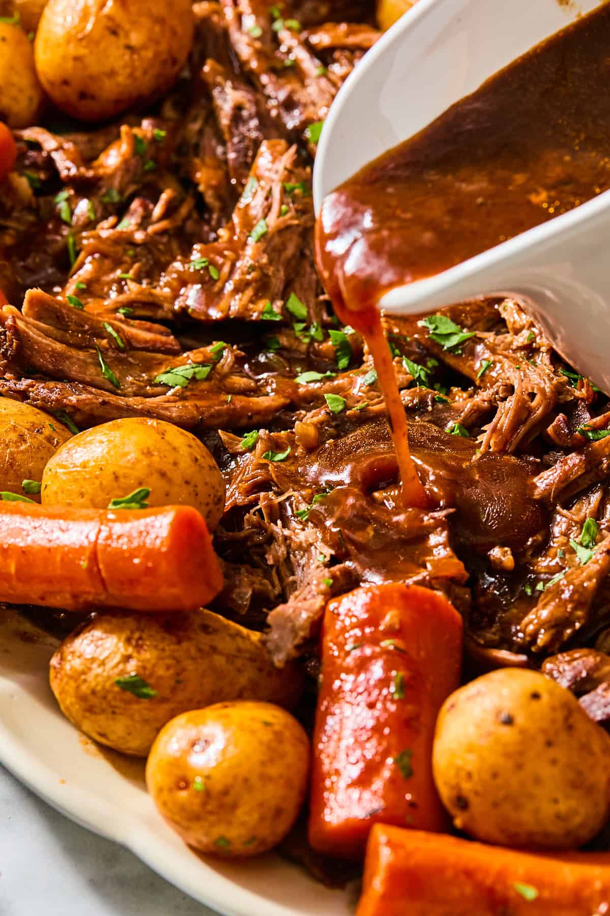 Pouring red wine gravy onto shredded beef, carrots, and potatoes.
