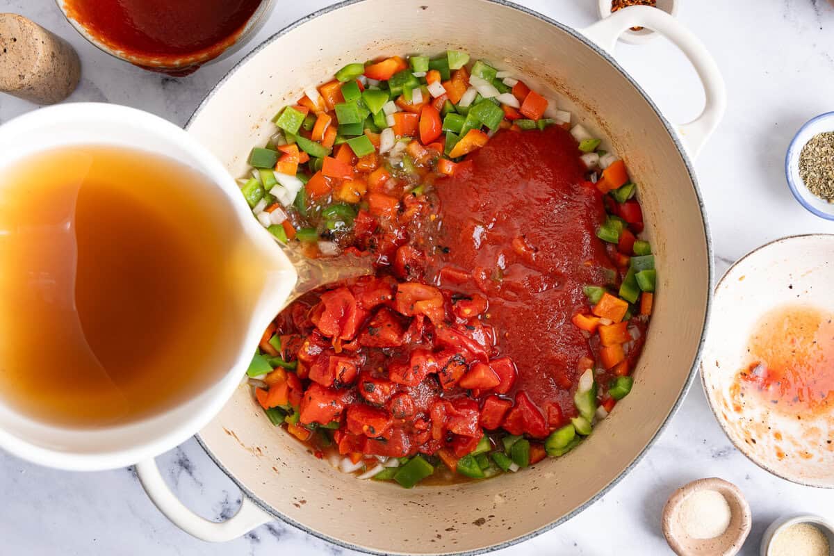 pouring broth, seasonings, and tomato paste into the sauteed veggies in a skillet