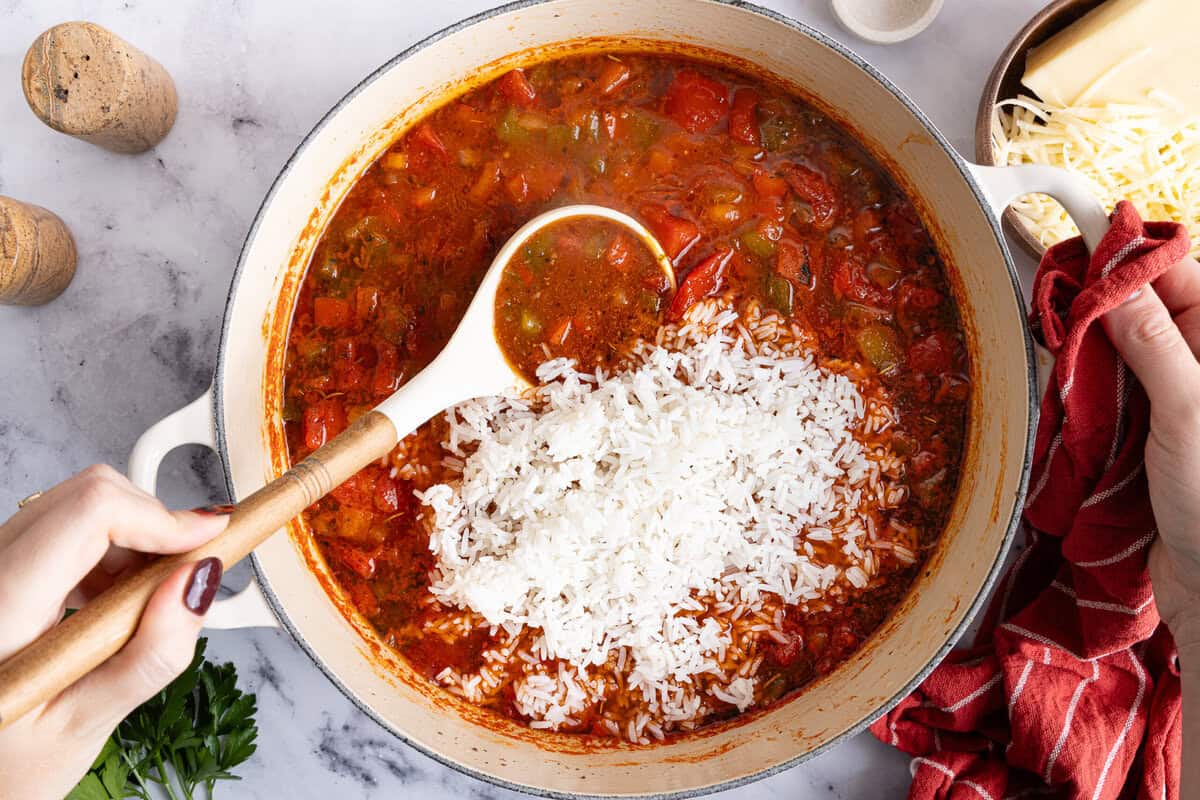 stirring cooked white rice into a soup pot of stuffed pepper soup