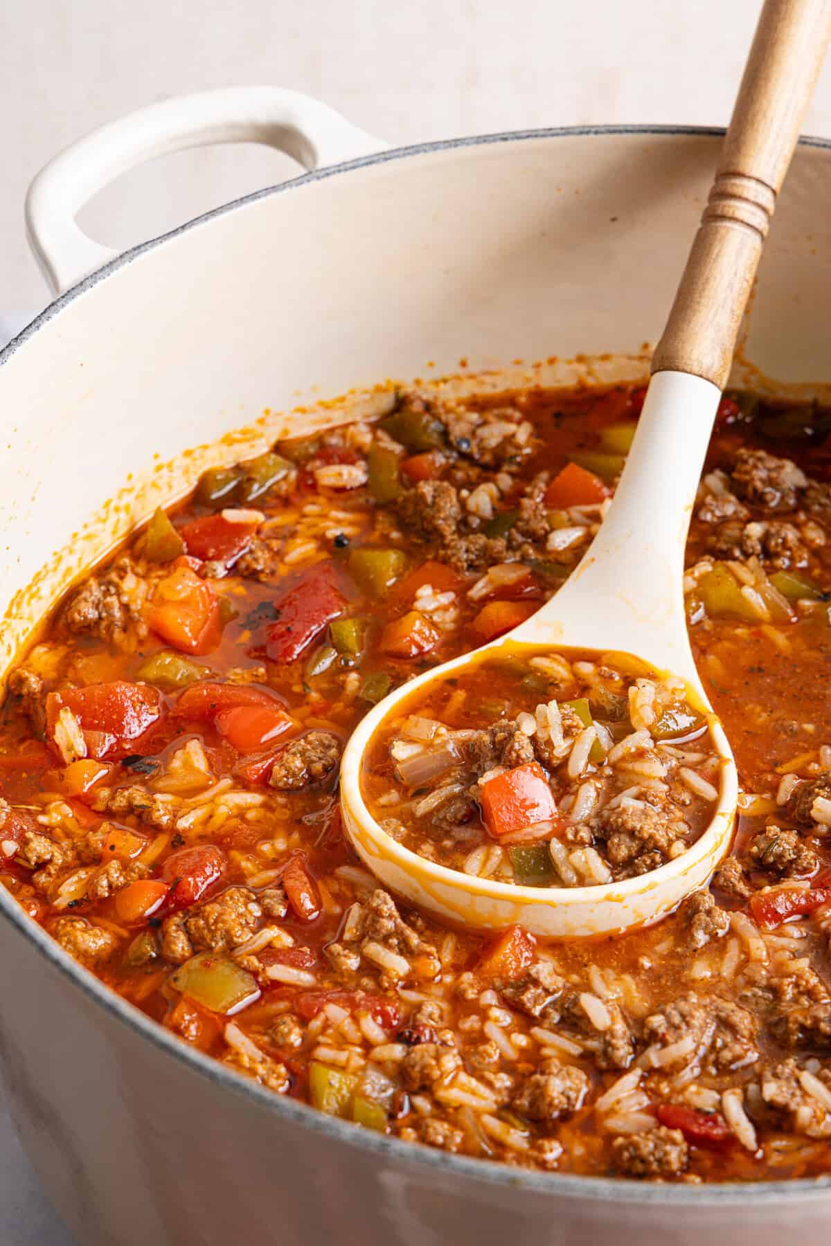 an up close photo of a ladle holding a scoop of stuffed pepper soup with rice, ground beef, and veggies.