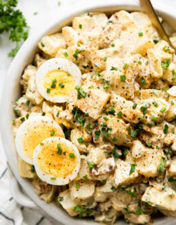a close up of a bowl of deviled egg whole30 potato salad tossed with chives and parsley with two sliced hard boiled eggs on top